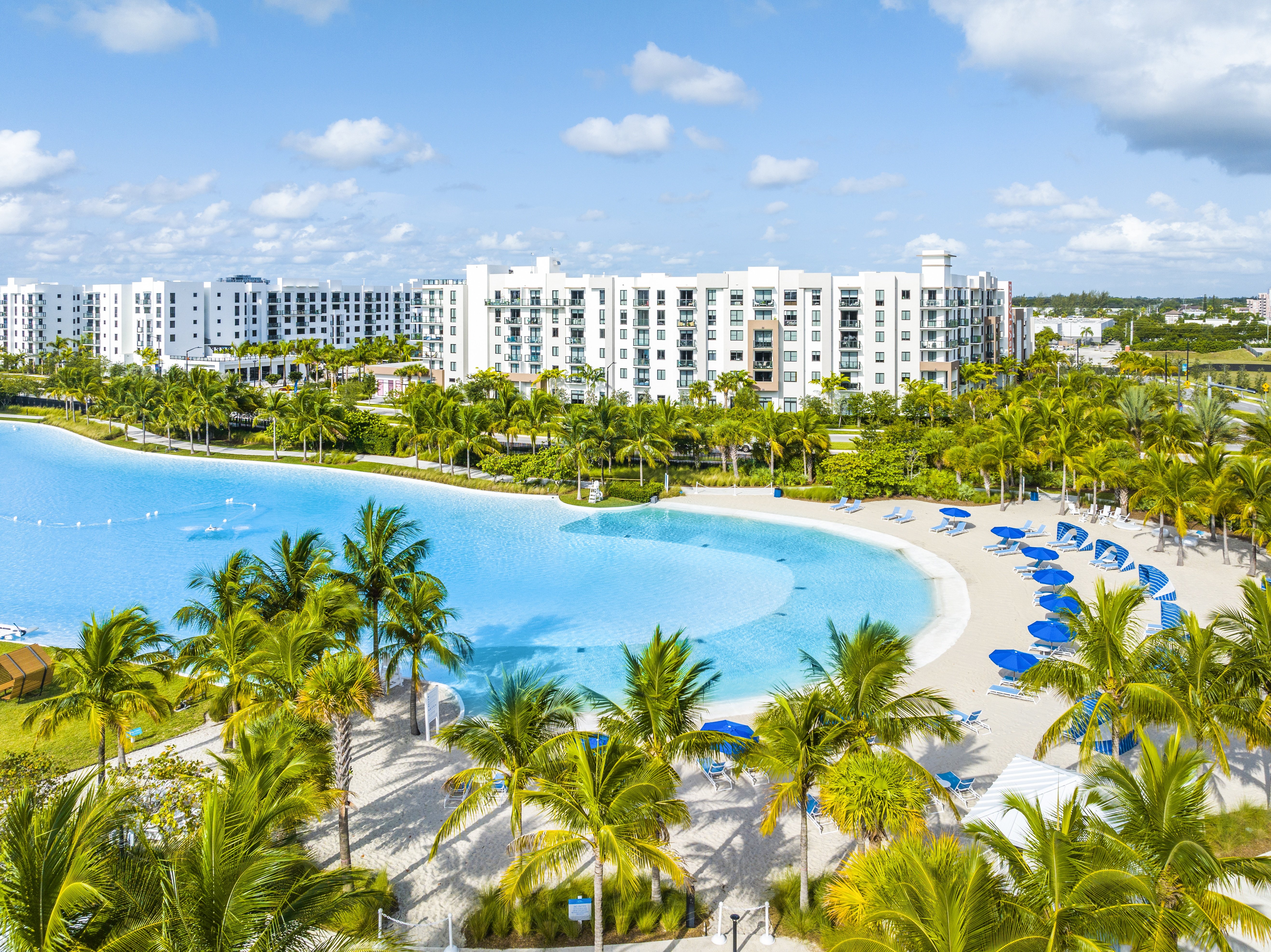 A large hotel with a pool surrounded by palm trees.